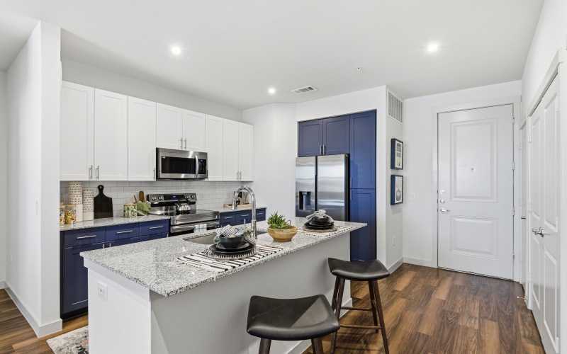 a kitchen with white and blue cabinets, kitchen island, stools, and wood floors