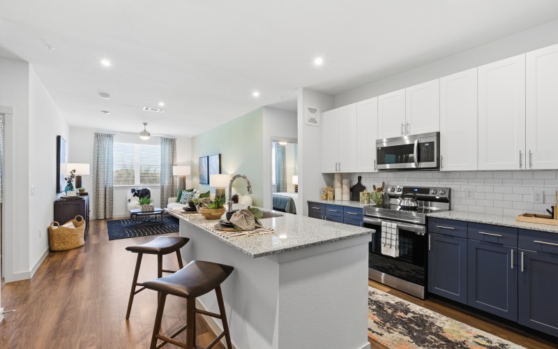 a kitchen with white and blue cabinets, kitchen island, stools, and wood floors