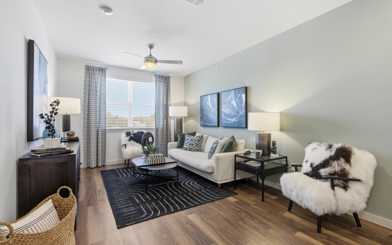 living room with green wall, large window, wood floors, rug, chair, two side tables and couch