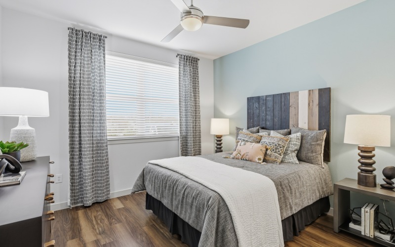 bedroom with wood floors, window, bed, table, lamp, ceiling fan